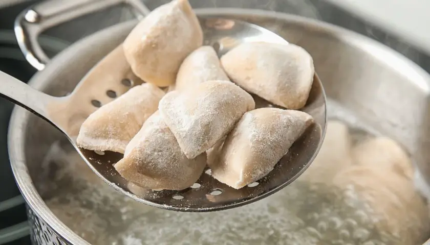 Mrożone pierogi na łyżce cedzakowej, gotowe do wrzucenia do wrzątku. Tak właśnie wygląda proces, jak rozmrażać pierogi.