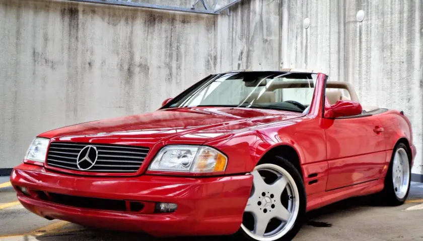 Czerwony kabriolet Mercedes-Benz SL500 z beżowym wnętrzem, zaparkowany przy betonowej ścianie.