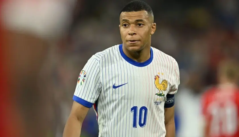 Kylian Mbappé w białej koszulce z numerem 10 i symbolem koguta, reprezentujący Francję. Jego obecne drużyny to PSG i reprezentacja Francji.
