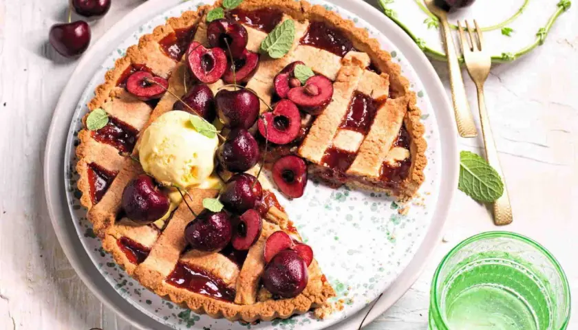 Una deliziosa crostata di ciliegie, guarnita con ciliegie fresche, gelato alla vaniglia e foglioline di menta. Perfetta per un dolce estivo.