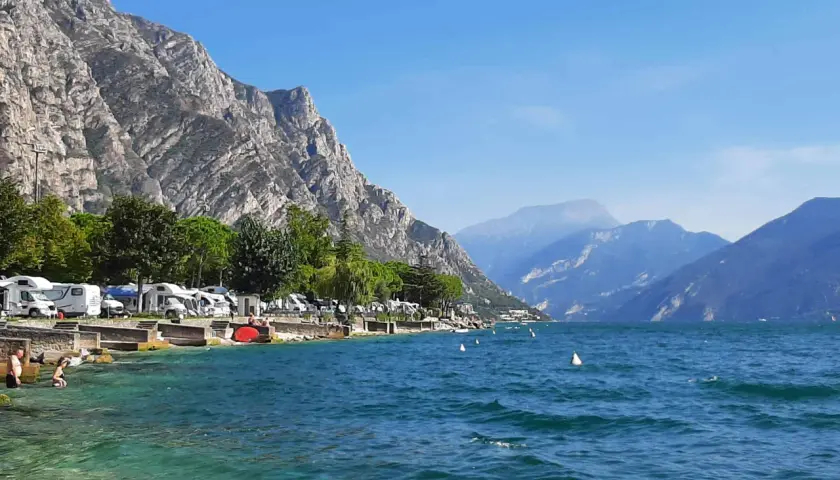 Malowniczy widok na jezioro Garda z campingiem, kamienistym brzegiem i górami w tle. Idealne miejsce na wakacje.