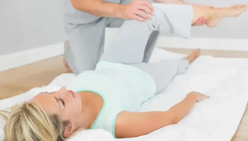 Fizjoterapeuta wykonuje test Patricka na leżącej kobiecie, delikatnie unosząc jej nogę.