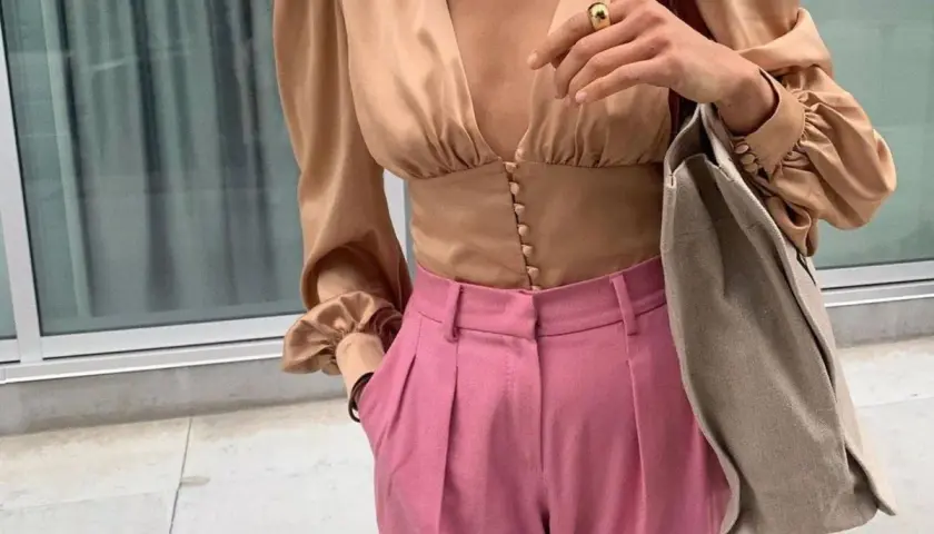 Elegante blusa beige satinada con pantalones rosa vibrante. Un look chic que demuestra los colores que combinan con el beige.