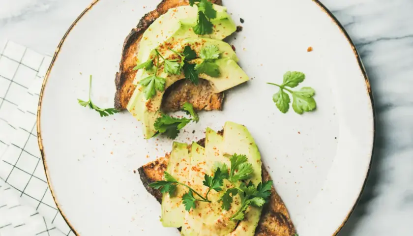 Deux toasts avec avocat tranché, persil frais et une pincée d'épices. Un avocat avec quoi, un délice simple et sain.