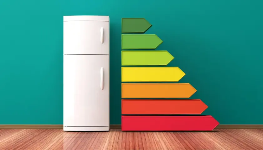 Biała lodówka obok kolorowej drabinki energetycznej pokazuje, ile prądu potrzebuje lodówka.