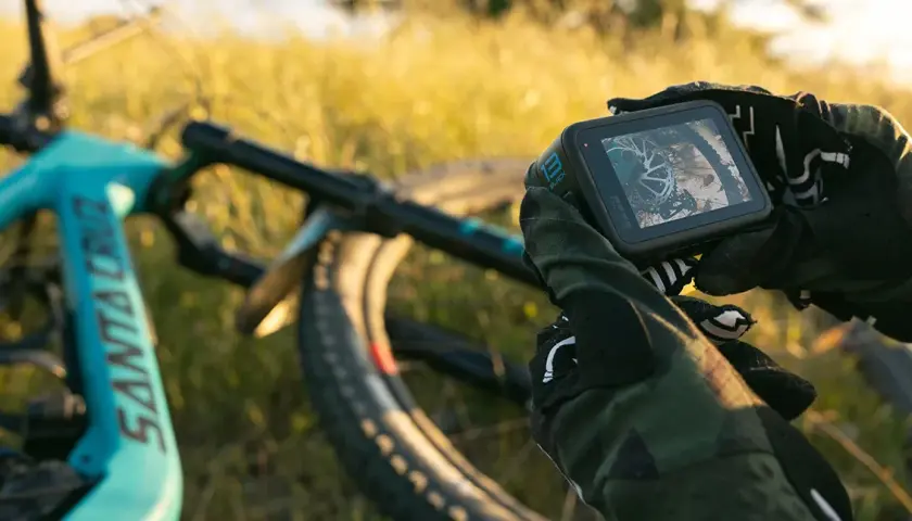 Ręce w rękawicach trzymają kamerę GoPro, gotową do nagrywania zjazdów na rowerze górskim. Niesamowite gopro zdjęcia czekają!