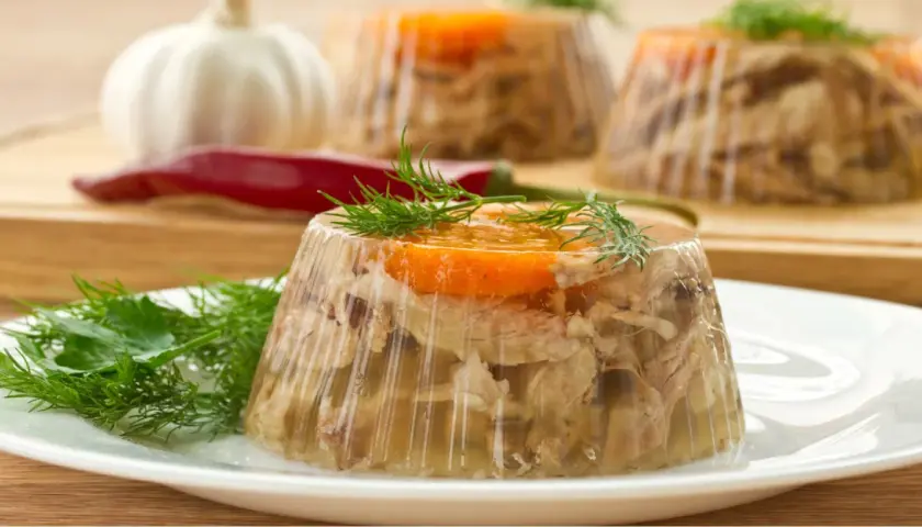 Gotowany schab w galarecie, ozdobiony marchewką i koperkiem, prezentuje się apetycznie na talerzu.