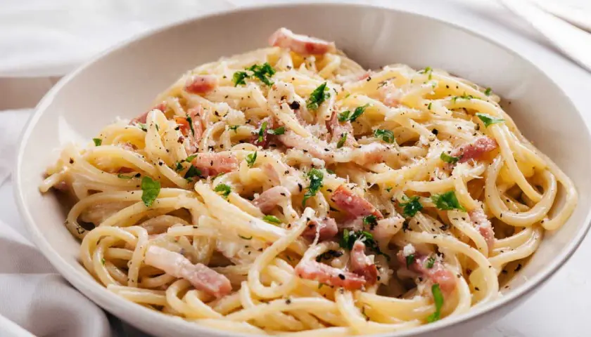 Un plat de pâtes à la carbonara crémeuses, garni de lardons, de parmesan râpé et de persil frais. Un délice italien.