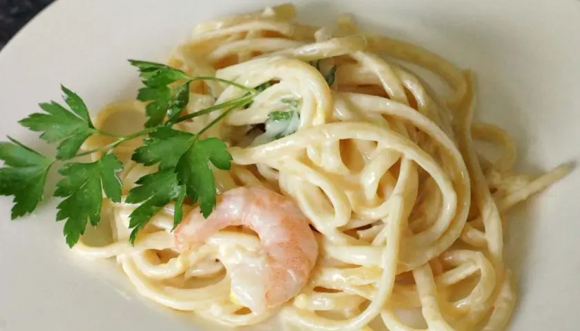 Cremige Pasta al Limone mit Garnelen und Petersilie auf einem weißen Teller. Ein Genuss für Augen und Gaumen.