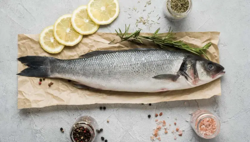 Lubina fresca, lista para cocinar. Un manjar de los pescados de temporada Galicia, acompañada de limón, romero y especias.