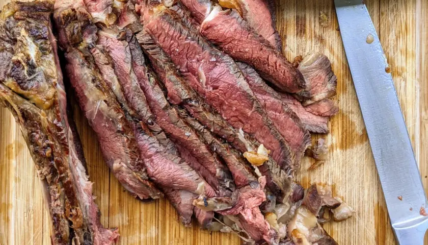 Tranches de bœuf juteuses, parfaitement cuites par la méthode du reverse searing, sur une planche en bois. Un couteau est à côté.