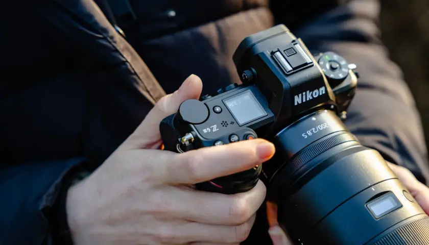 Dłonie trzymają aparat Nikon Z6 III z obiektywem.