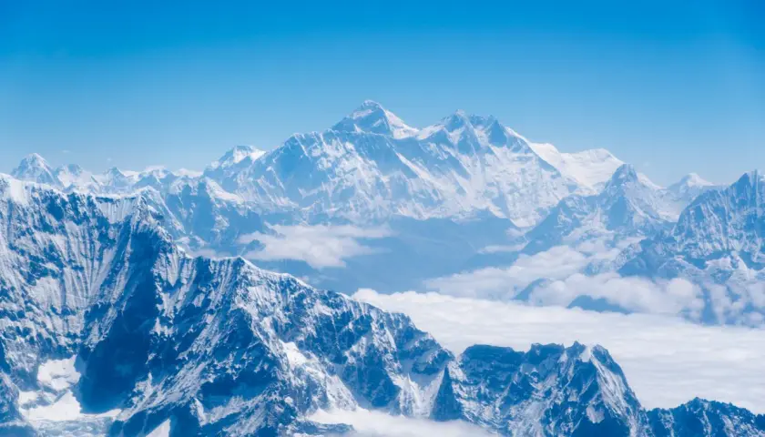 Majestatyczne, ośnieżone szczyty Himalajów, gdzie leży Mount Everest, wyłaniają się z morza chmur pod błękitnym niebem.