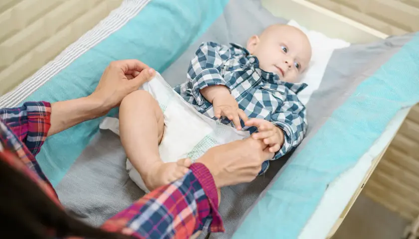 Mama zmienia pieluszkę maluszkowi. Dobór odpowiednich rozmiarów pampersów jest kluczowy dla komfortu dziecka.