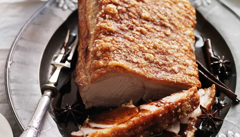 Poitrine de porc croustillante, dorée et juteuse, servie sur une assiette ornée avec des épices.