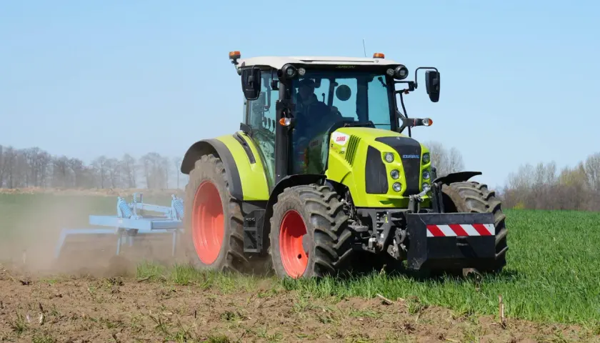 Zielony traktor Claas Arion 430 pracuje na polu, spulchniając ziemię.