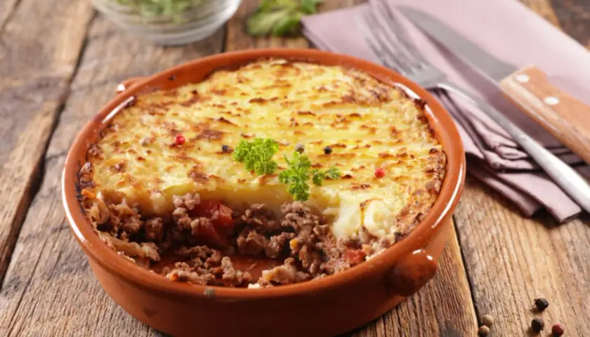 Un plat de hachis parmentier, un classique du repas français, servi dans un plat en terre cuite sur une table en bois.