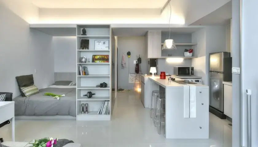 Nowoczesne mieszkanie 38 m2 aranżacja: łóżko, regał, aneks kuchenny z wyspą i lodówką. Jasne, minimalistyczne wnętrze.