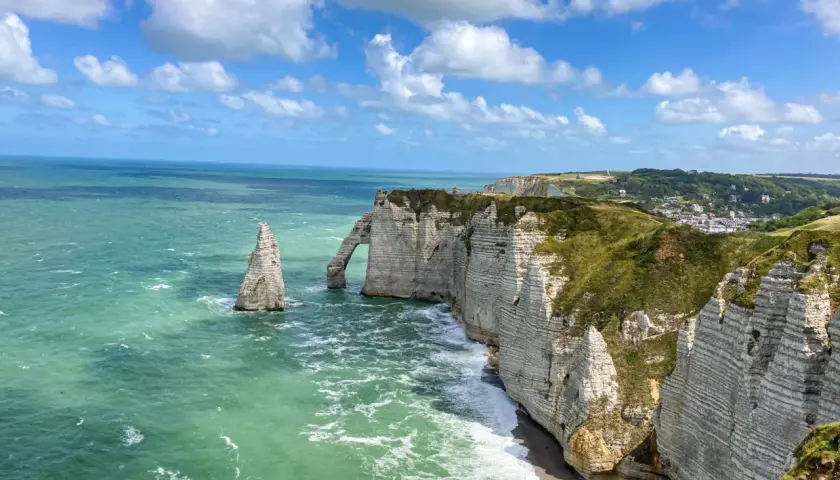Klify w Étretat, Normandia: białe skały, łuk skalny i iglica w zielonym morzu.