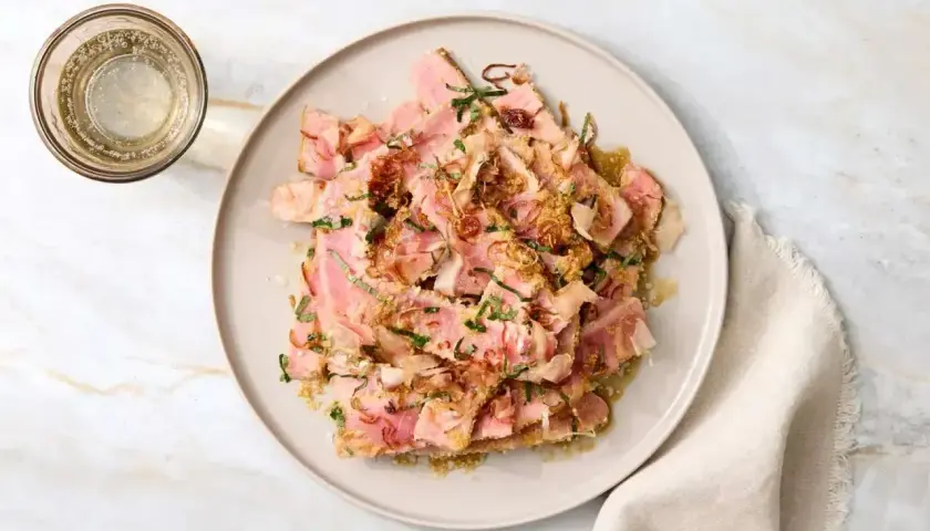 Tataki z ryby na talerzu, posypane ziołami i chrupiącą cebulką, obok szklanka napoju.