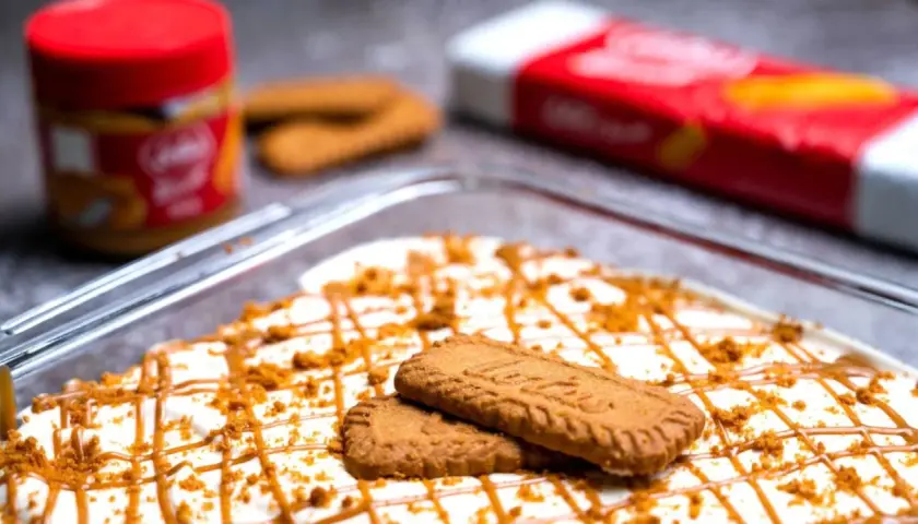 Postre cremoso decorado con galletas y caramelo, con un tarro y paquete de **lotus biscoff ingredients** al fondo.