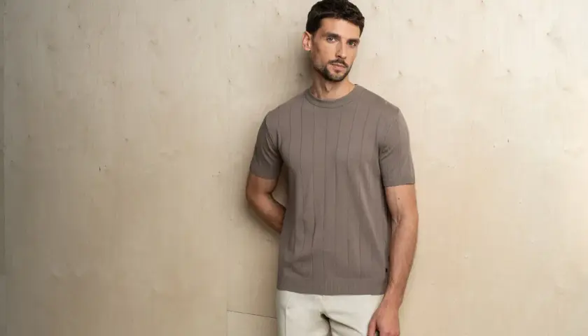 Mężczyzna prezentuje elegancki, casualowy styl. Brązowa, prążkowana koszulka z krótkim rękawem i beżowe spodnie tworzą harmonijną całość.