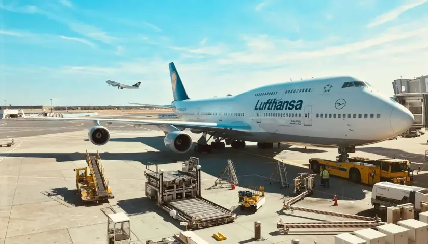Lufthansa bagaż podręczny czeka na załadunek obok gigantycznego Boeinga 747-400 na lotnisku.