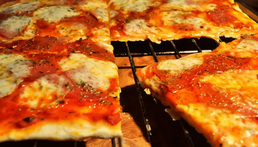 Pyszna pizza na cienkim cieście, z sosem pomidorowym i ciągnącym się serem, pokrojona na kwadraty.