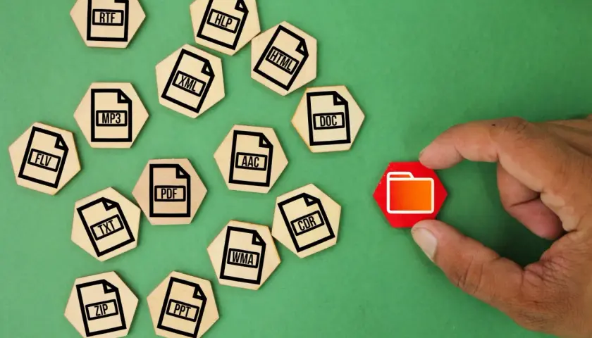 Un dedo toca una carpeta roja, rodeada de fichas de madera con extensiones de archivo como ZIP, MP3, DOC, etc. que representan un archivo comprimido.