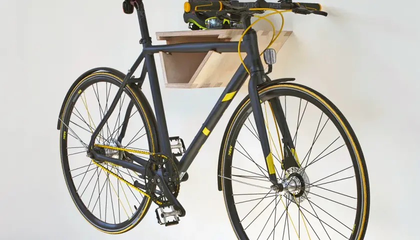 Schwarzes Fahrrad mit gelben Akzenten hängt an einer selbstgebauten Holz-Fahrrad-Wandhalterung. Helm liegt auf der Ablage.