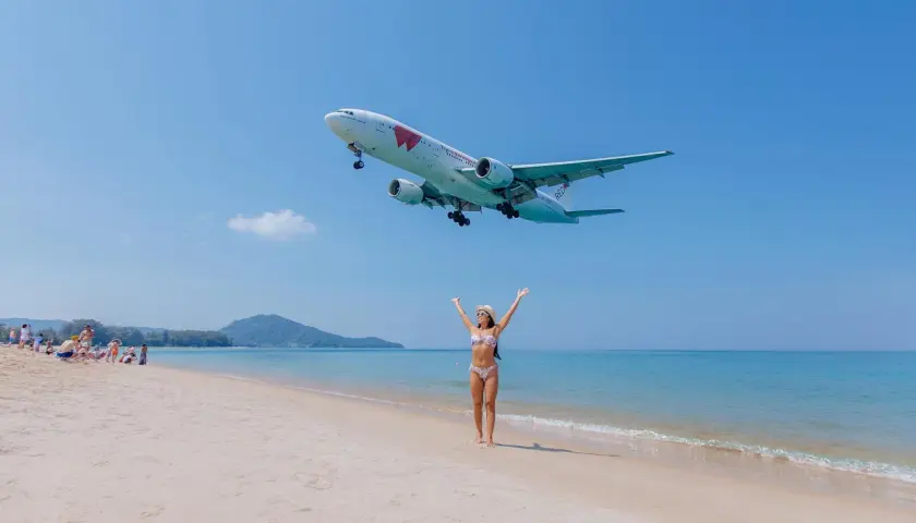 Frau am Strand jubelt, als ein Flugzeug landet. Der Traum vom Urlaub in Thailand wird mit dem Visum Thailand wahr.