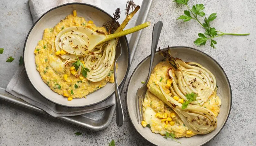Deux bols de polenta crémeuse avec du fenouil rôti, du maïs et du persil.