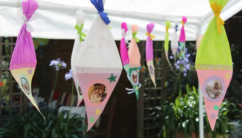 Bunte Zuckertüten mit Fotos hängen im Garten. Perfekte Spiele zur Einschulung im Garten für einen unvergesslichen Tag.