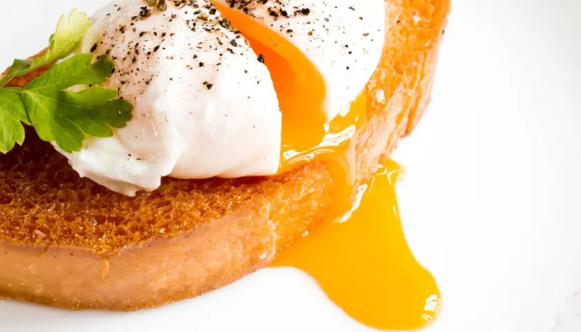 Un œuf mollet parfait, avec son jaune coulant, sur une tranche de pain grillé. Le temps de cuisson est idéal pour ce délice.