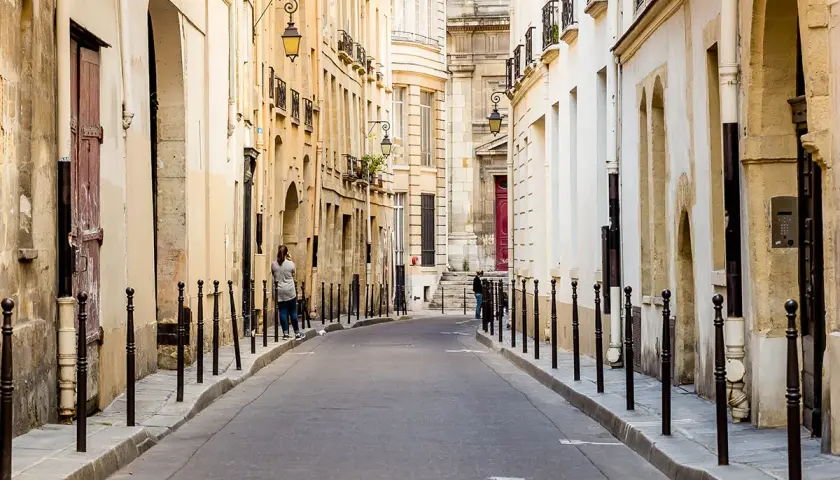 Urokliwa uliczka w paryskiej dzielnicy Le Marais, z kamiennymi budynkami i latarniami.