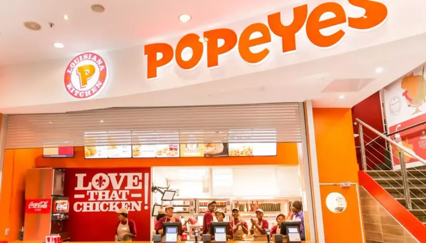 Wnętrze restauracji Popeyes Polska. Pracownicy za ladą, logo "Love That Chicken" i menu.