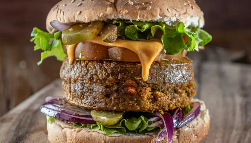 Deliciosa hamburguesa vegana con queso derretido, lechuga fresca, pepinillos y cebolla morada.