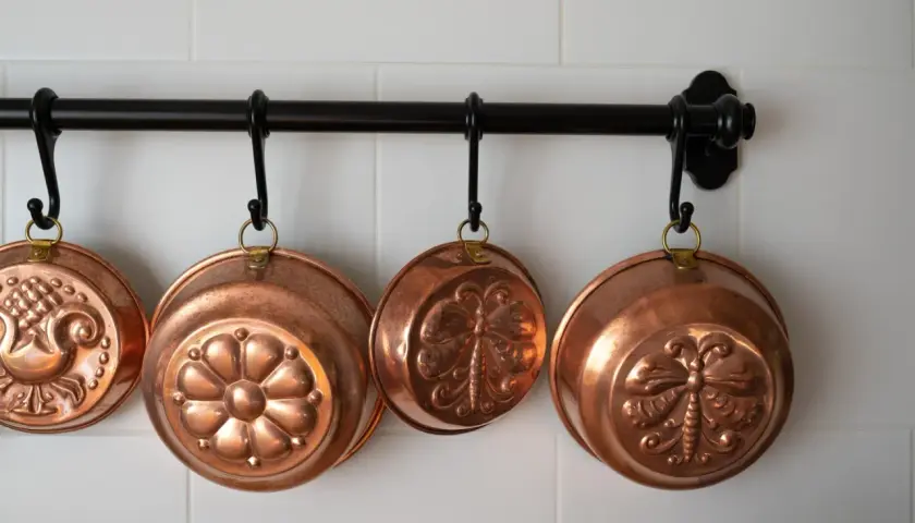 Cuencos de cobre decorados cuelgan de una barra. Aprende como limpiar cobre para que brillen así.