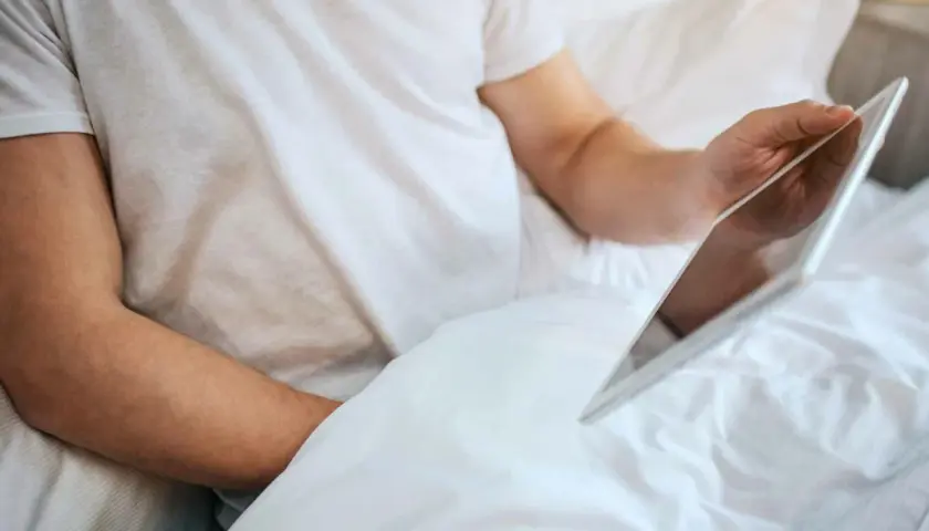 Persona in letto con tablet, forse cercando informazioni su che significa masturbare.