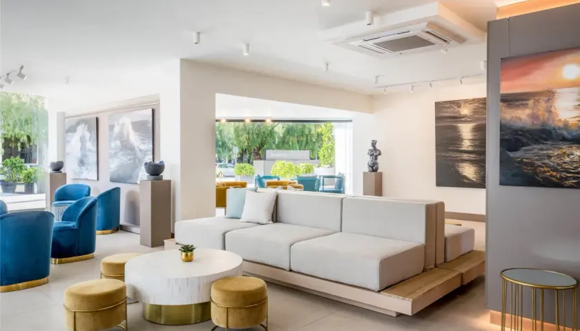 Salón moderno con sofás modulares, sillones azules y arte marino. El cartel "Occidental Puerto Banús" se ve al fondo.