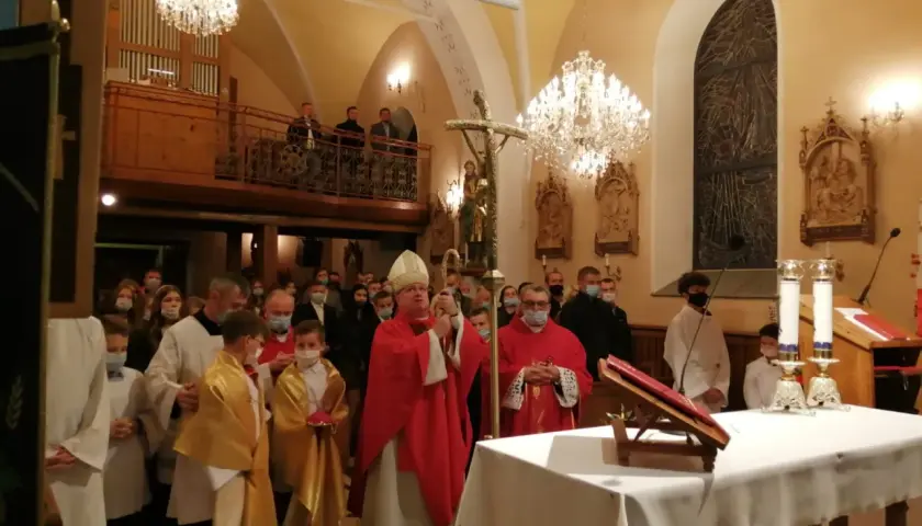 Biskup w czerwonej szacie, który jest szafarzem bierzmowania, błogosławi wiernych w kościele.