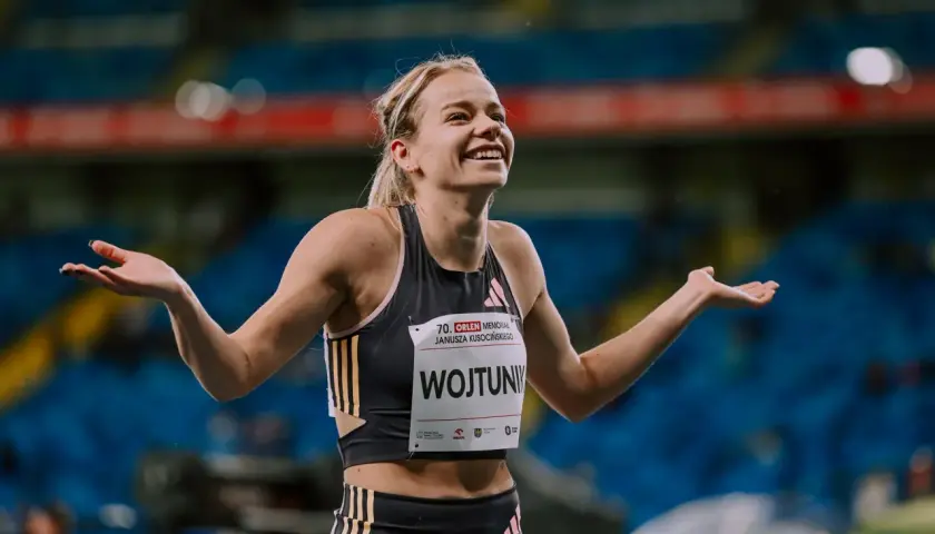 Uśmiechnięta Klaudia Wojtunik z rozłożonymi rękami na stadionie, celebrująca sukces.
