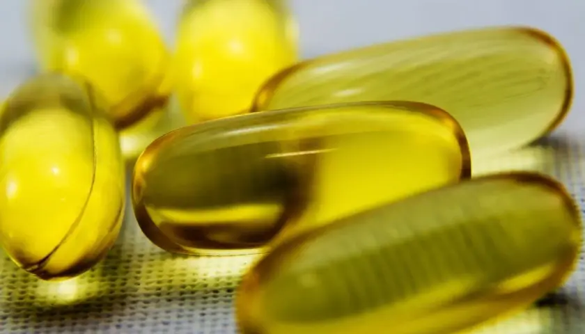 Kilka żółtych kapsułek z płynem, zawierających cenne kwasy omega 3, leży na białej powierzchni.