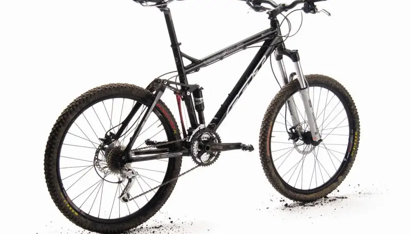 A black full-suspension mountain bike, the "Felt Virtue," stands ready for adventure. Its knobby tires are dusted with dirt, hinting at recent trails.