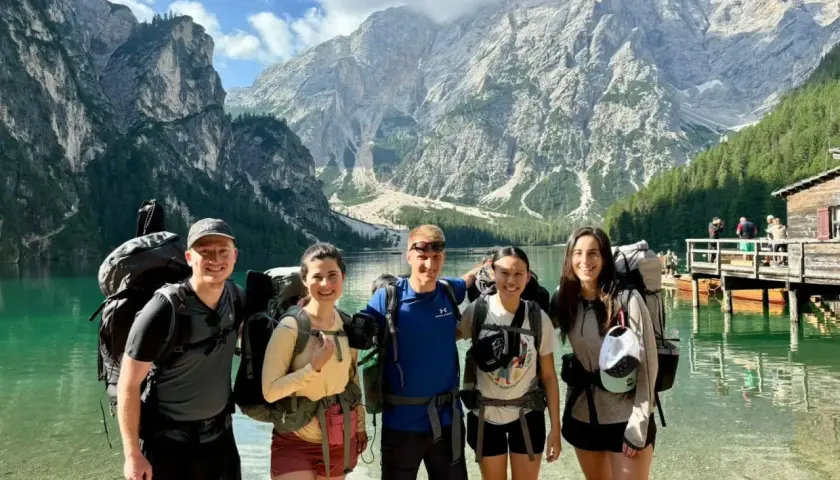 Cinco excursionistas sonríen junto a un lago turquesa con imponentes montañas de **Alta Ribagorza** al fondo.