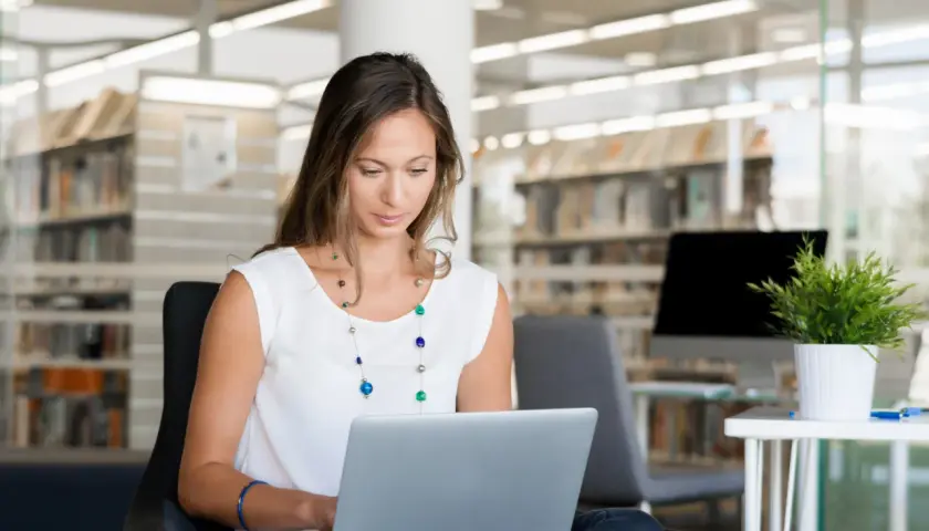 Kobieta siedzi w bibliotece, ucząc się, jak założyć PUE ZUS na laptopie.