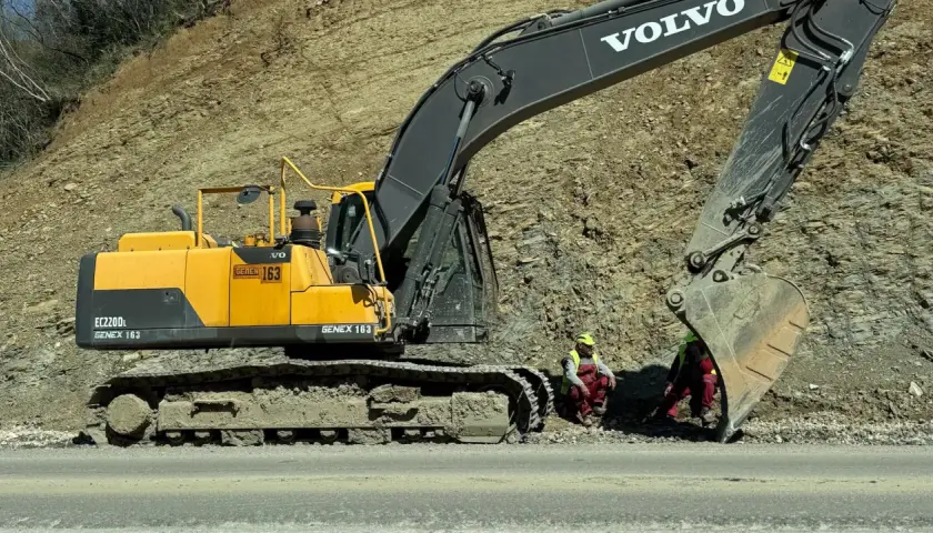 Dwa rodzaje koparek, w tym żółta Volvo EC220DL, pracują przy osuwisku. Dwóch robotników w kamizelkach odblaskowych odpoczywa.