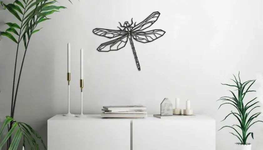 Un moderno cuadro de libélula adorna la pared blanca, sobre un mueble blanco con plantas y velas.