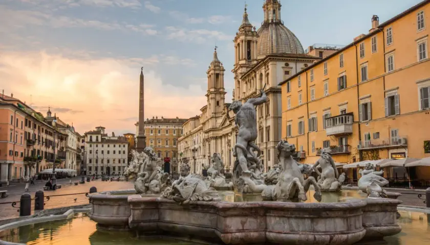 Fontana dei Quattro Fiumi a Piazza Navona, con l'obelisco e la chiesa di Sant'Agnese in Agone sullo sfondo, al tramonto.