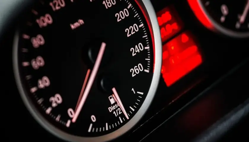 Zbliżenie na deskę rozdzielczą samochodu: prędkościomierz pokazuje 80 km/h, a obok wskaźnik paliwa wskazuje prawie pełny bak.